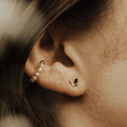 Gold butterfly mini stud worn on an ear beside pearl studs