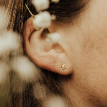Gold flower stud earring with a delicate openwork petal design, worn on the earlobe.