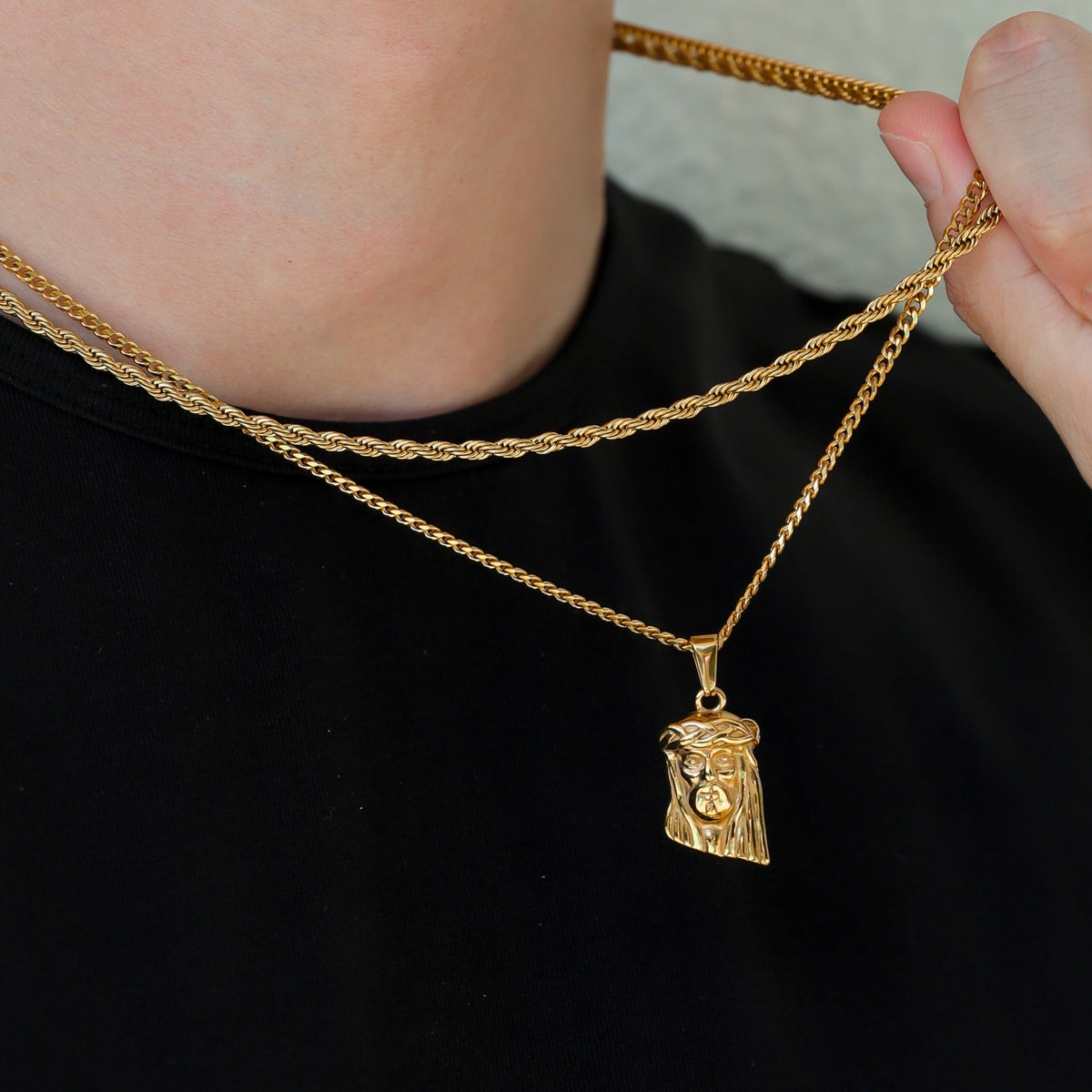 Gold chain necklace with Jesus face pendant charm, close-up held by hand