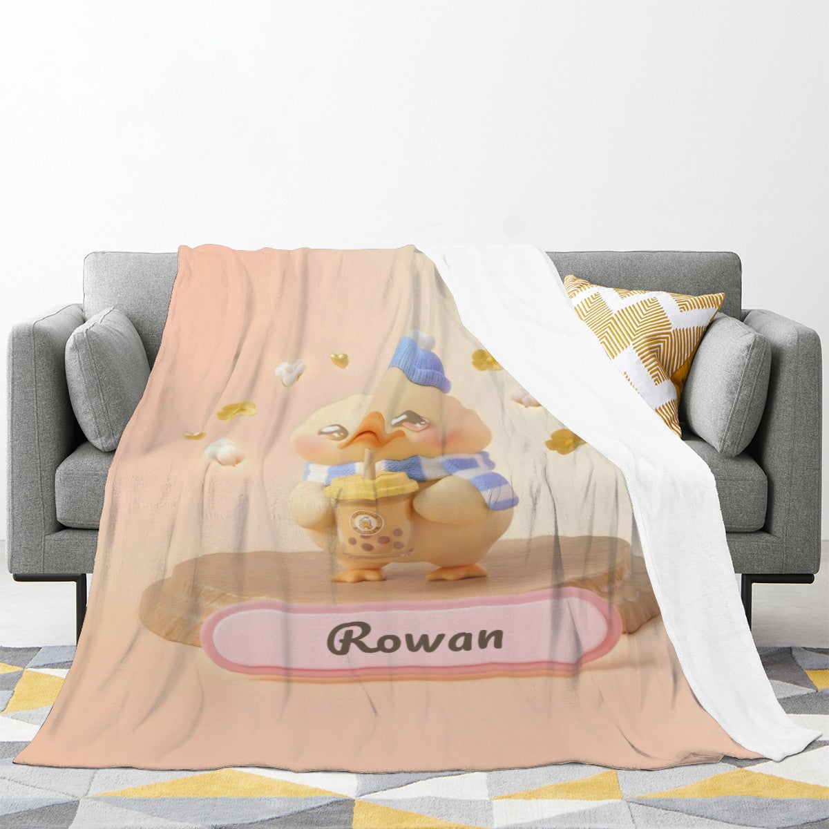 Light beige duck character blanket draped over sofa with blue hat and ribbon name badge