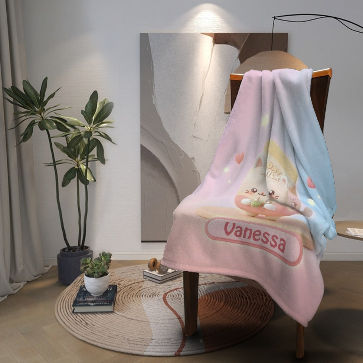Pastel pink-and-blue blanket with bunny graphic and “Vanessa” band, folded on chair