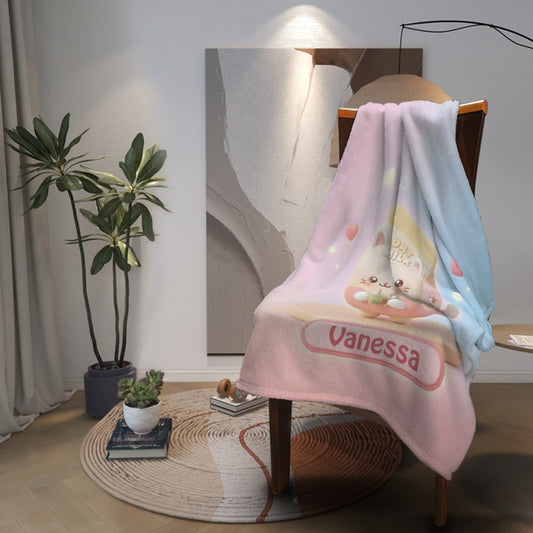 Pastel pink-and-blue blanket with bunny graphic and “Vanessa” band, folded on chair