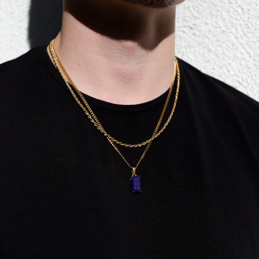 Gold-tone chain necklace with blue rectangular stone pendant, worn against black shirt