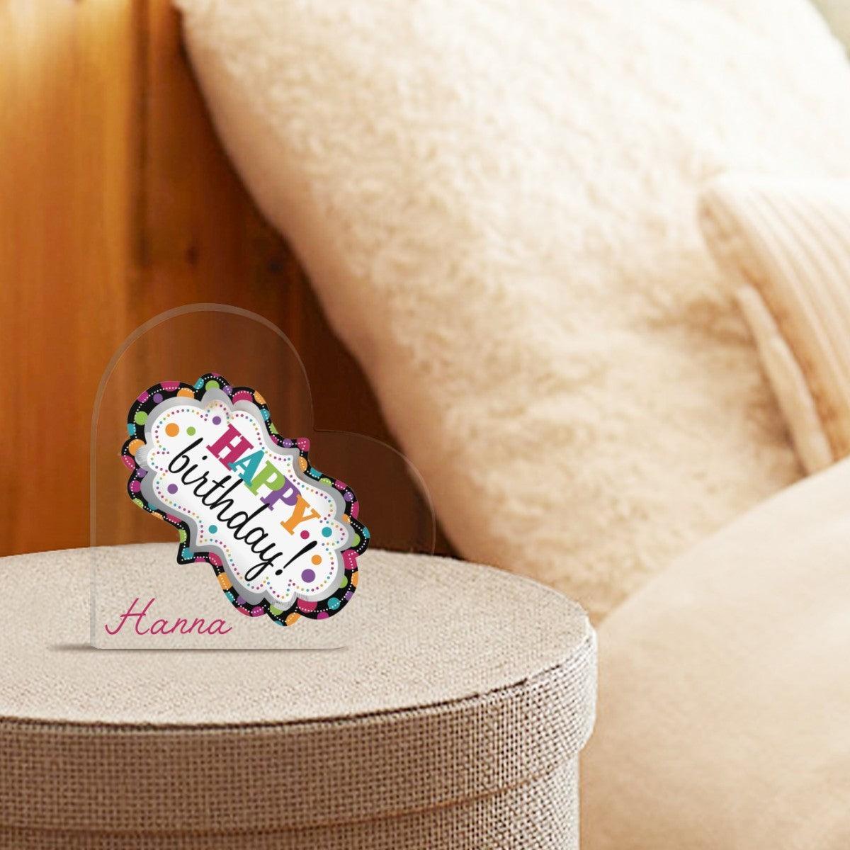 Acrylic heart ornament with Happy Birthday Hannah on a fabric surface