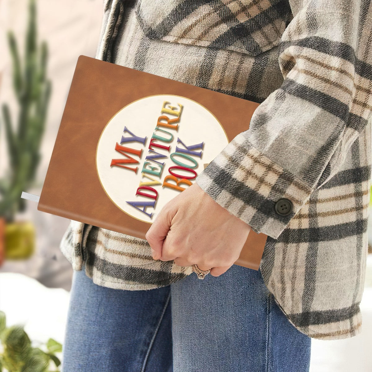 Brown faux-leather notebook held by hand with “My Adventure Book” emblem