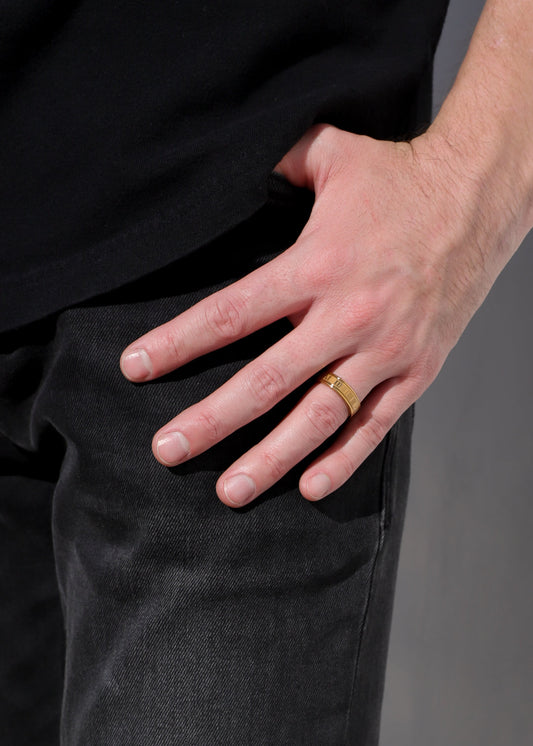 Gold-tone ring band with roman numerals on a hand over dark pants
