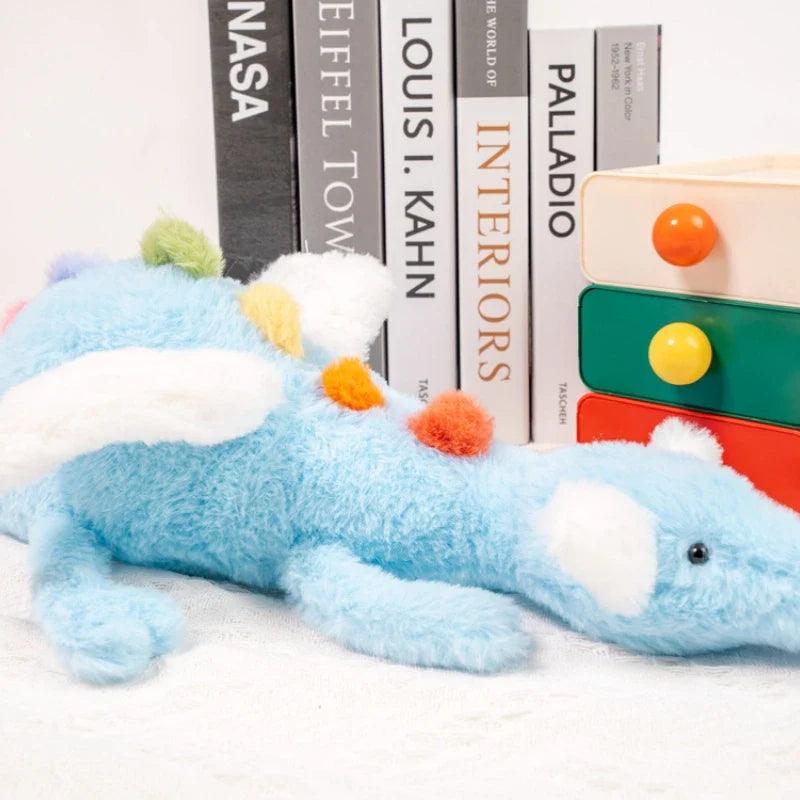 Rainbow dragon plush toy lying down, light blue plush with orange pom details and black eye