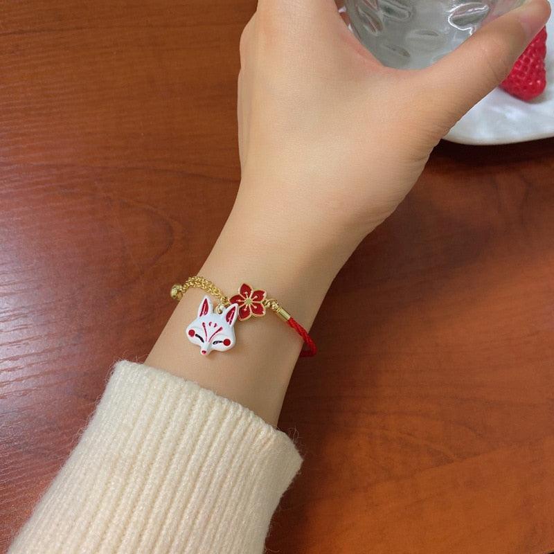 Fox charm bracelet with red cord, gold chain, and fox head charm on wrist