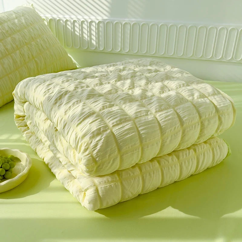 Light yellow seersucker duvet cover set folded on bed with matching pillow shams