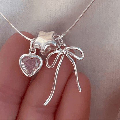Silver heart and bow charm necklace detail with pink heart stone and ribbon loops