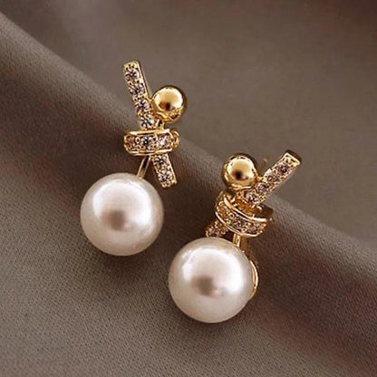 Gold-tone pearl charm earrings with dangling white pearls and glitter bow accents
