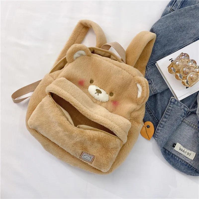 Light tan plush bear backpack laid flat, showing bear face front pocket and side strap