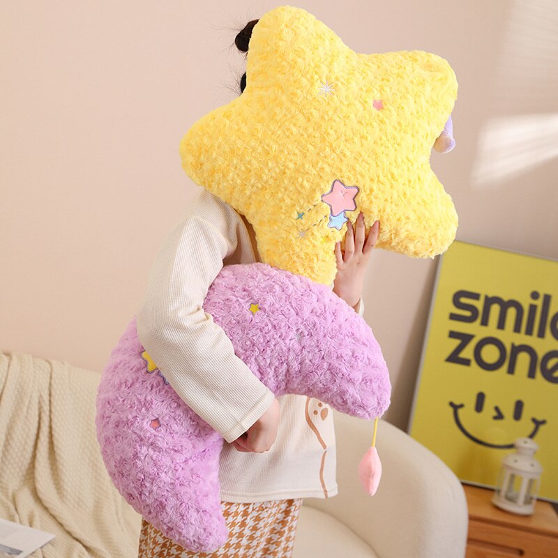 Plush star and crescent moon pillows in yellow and purple, gripped by hands