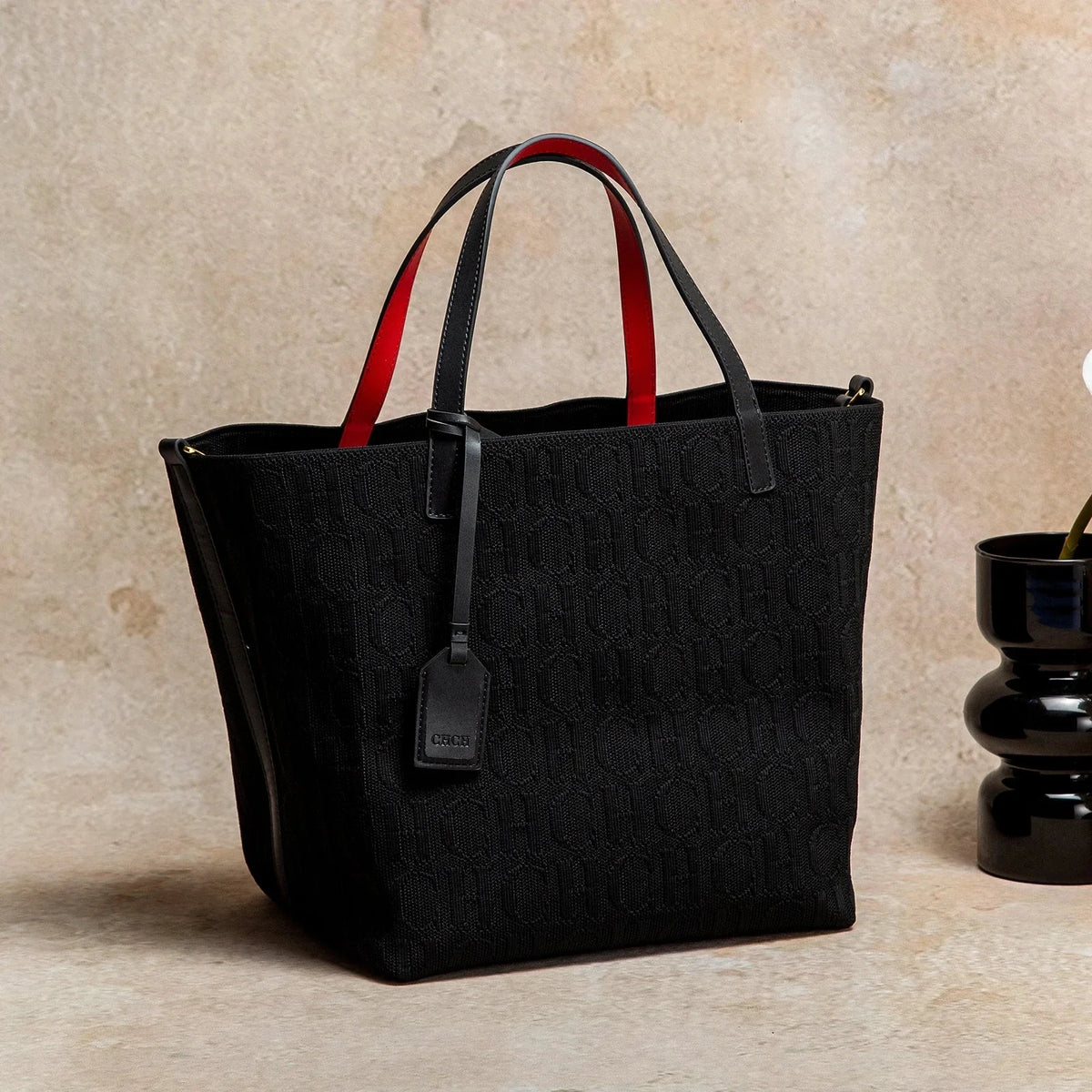 Black knitted tote bag with embossed CHCH pattern, top handles, front hanging tag.