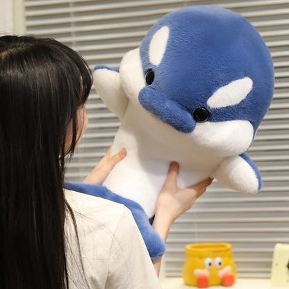 Blue and white dolphin plush held by a person, front face with white fin patches.