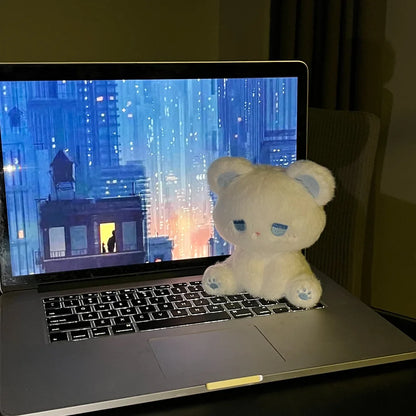 White plush cat with blue sleepy face sitting near a laptop, soft stuffed toy