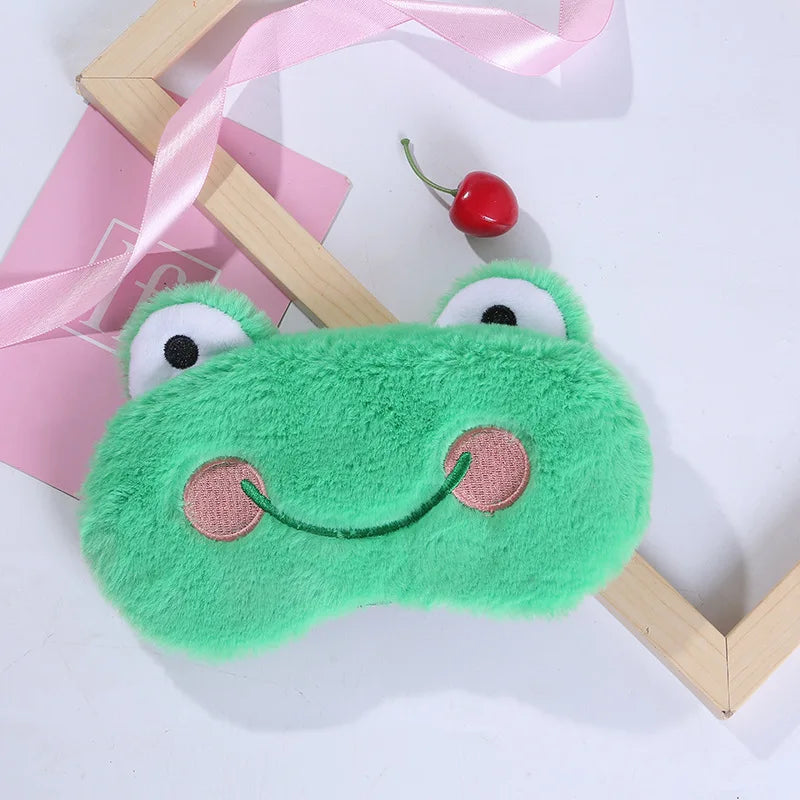 Green frog plush sleep mask with smiling stitched face, round eyes, and soft textured fabric
