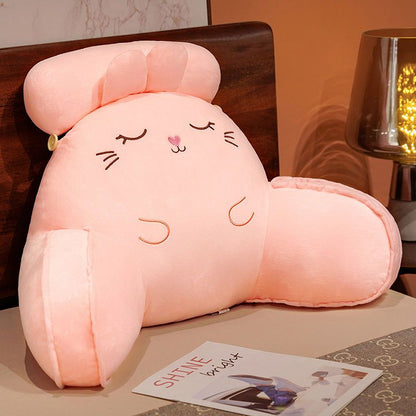 Pink plush reading pillow with closed-eye cat face, heart nose, and rounded arms
