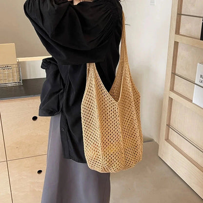 Beige knitted crochet tote bag with long handles, hanging at side