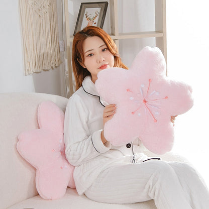 Pink cherry blossom plush pillow tucked against person’s chest, embroidered stamen petals