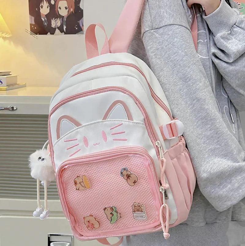 Pink and white cat-face school backpack worn on shoulder with hanging pom keychain