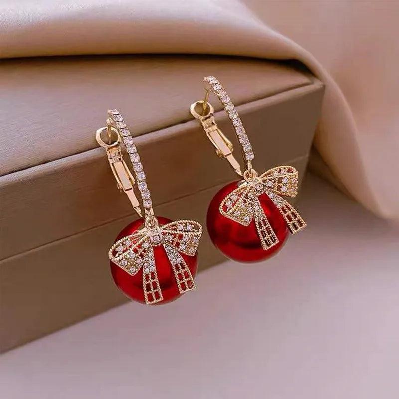 Gold-tone hoop earrings with red bauble and rhinestone bow charm