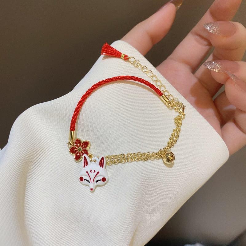 Red string bracelet with gold chain, fox head charm, and tassel detail