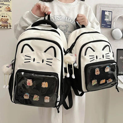 Two white cat backpacks with black trim; front clear pouch with colorful patches, straps on.