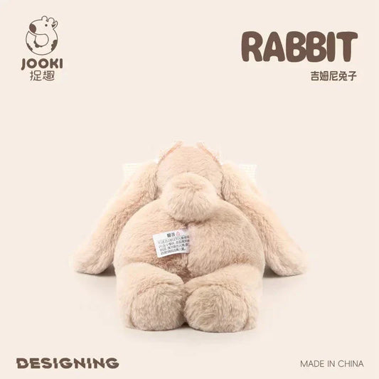 Beige plush rabbit toy, sitting pose, small white fabric tag on belly.