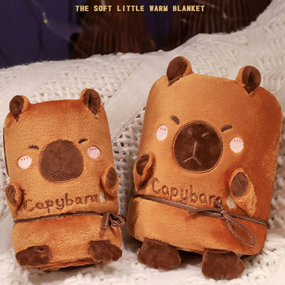 Rolled capybara-shaped blanket pillow pair, orange plush with stitched face and paws.
