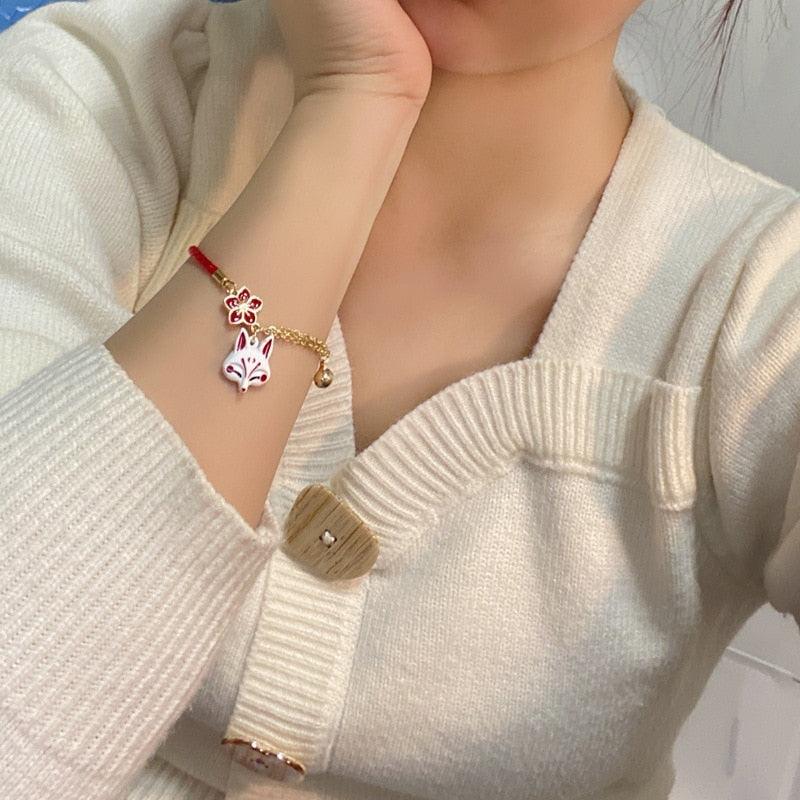 Fox head charm bracelet with red cord and gold chain, worn with a knit sweater