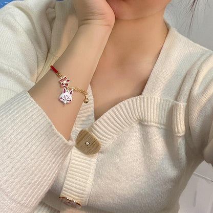 Fox head charm bracelet with red cord and gold chain, worn with a knit sweater