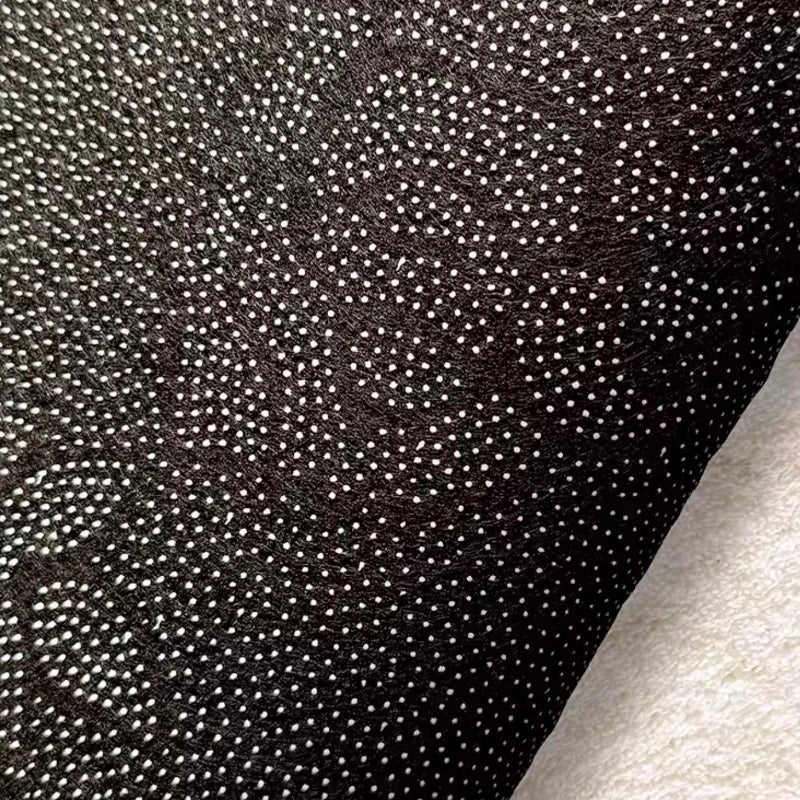 Dark speckled rug backing fabric close-up with dense woven texture.