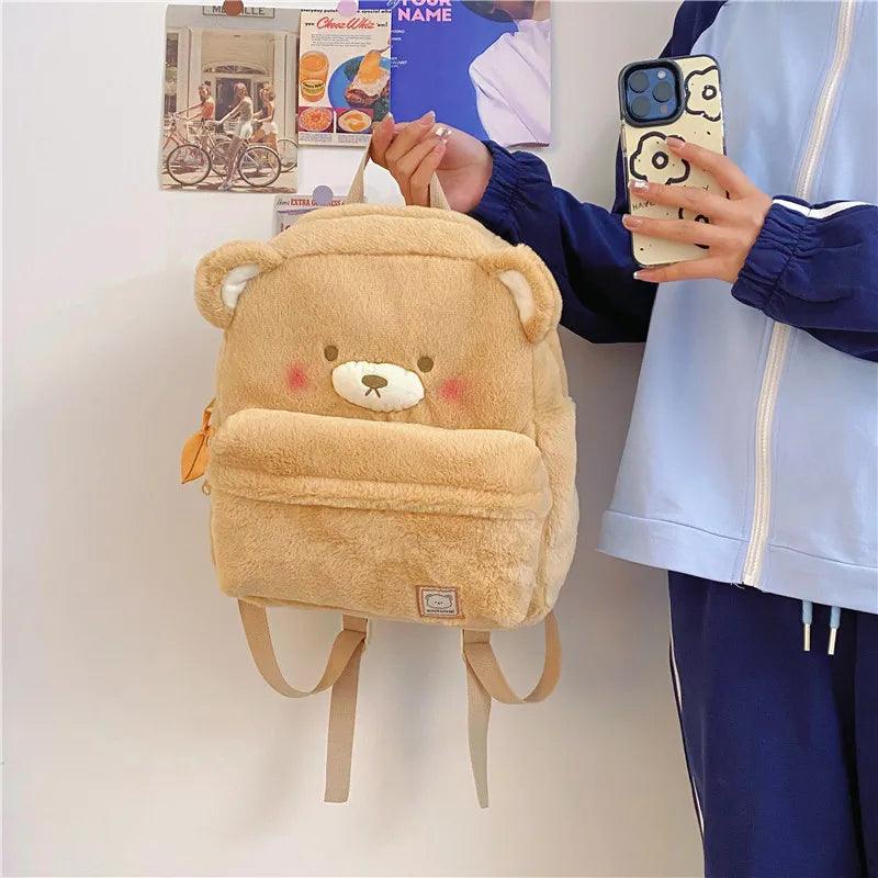 Light tan plush bear backpack front view with bear face patch and dangling bottom straps