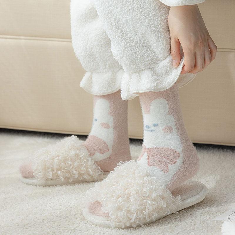 Bunny socks on feet with fuzzy white fabric and pastel pink-and-blue paw print pattern.
