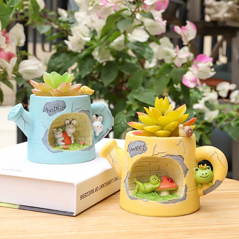 Resin watering can plant holders with blue and yellow pots, each holding a succulent