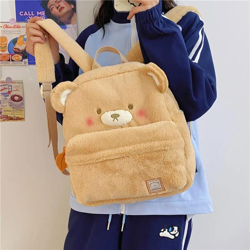 Light tan plush bear backpack worn, featuring bear face patch and rectangular front label