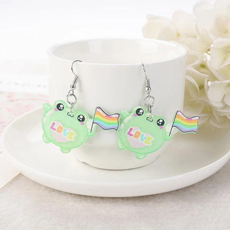 Frog acrylic earrings with green frog charms, rainbow flag accessory, and silver hooks
