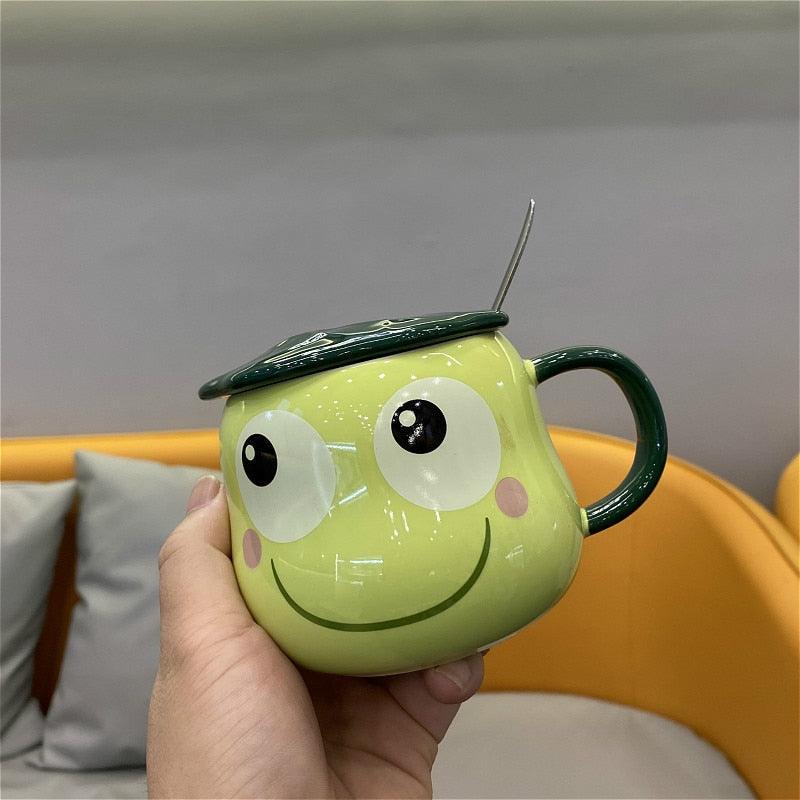 Lime green frog-shaped mug with lid and spoon, held in hand, green handle and smiling face