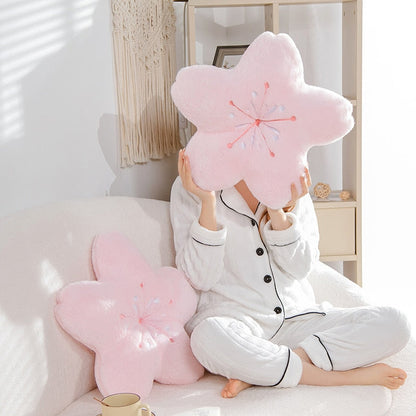 Pink cherry blossom plush pillows on couch, person holding one embroidered flower cushion