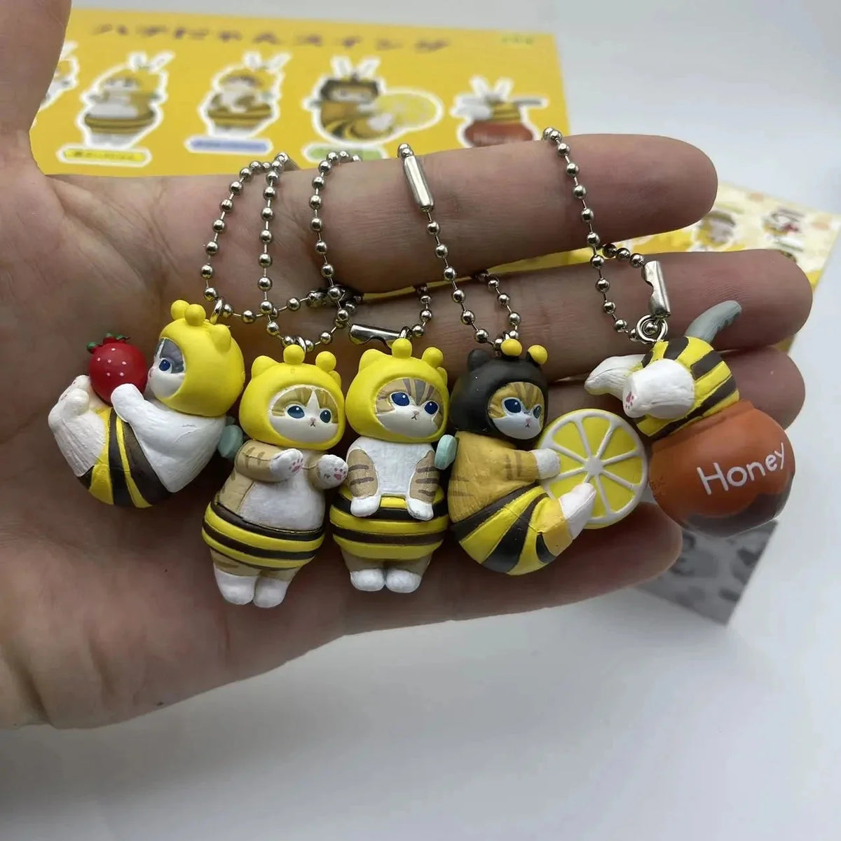 Hand holding bee-shaped twisted egg figure keychain charms with silver bead chains