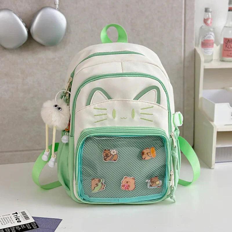 White cat school backpack with green trim; front mesh pocket with small cartoon patches.