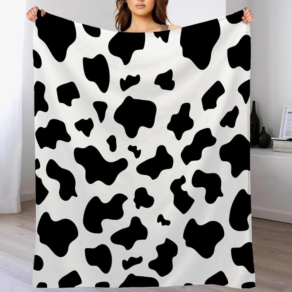 Cow print flannel blanket in black and white, held up for display