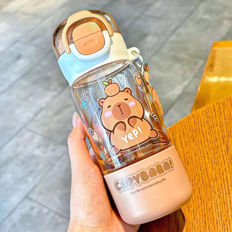 Capybara-themed water bottle held in hand, clear body, white cap and orange latch, bear graphics