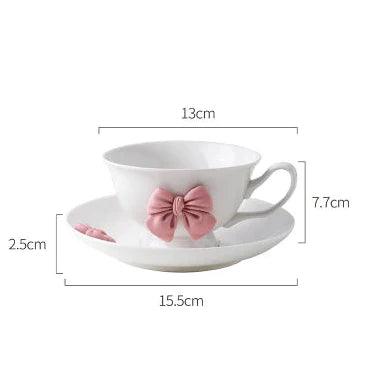 White teacup and saucer set with pink bow decoration and right-side handle