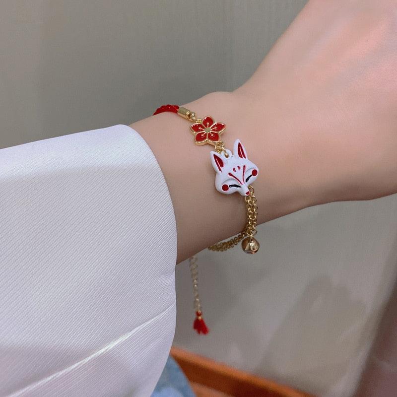 Red cord and gold charm bracelet with fox head, red flower, and small bell