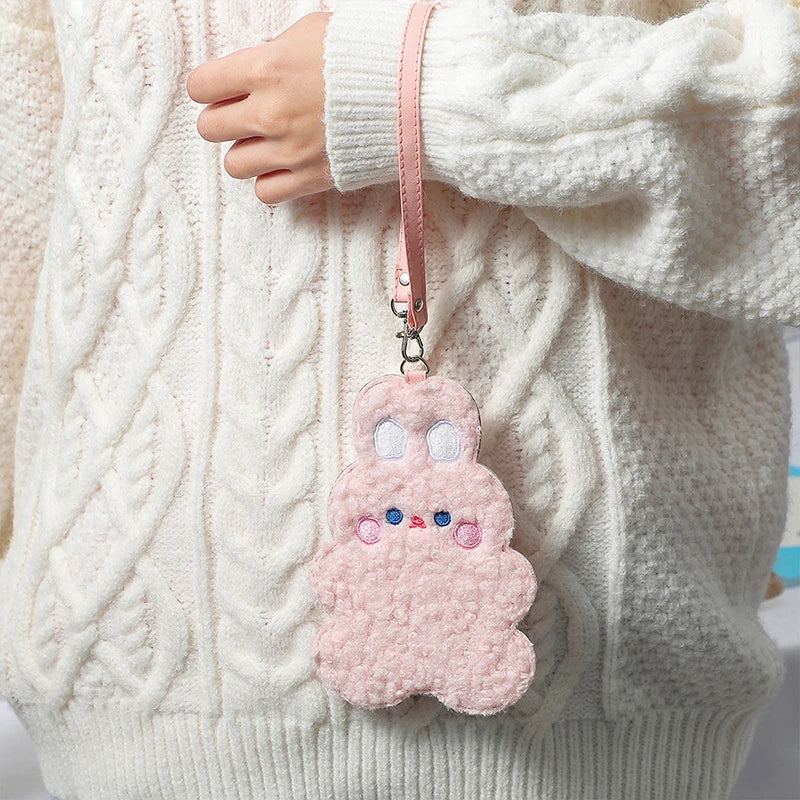 Pink plush animal photo card sleeve on strap worn over a white cable-knit sweater