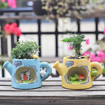 Resin watering can plant holders on a bench with green saplings and bunny/frog faces