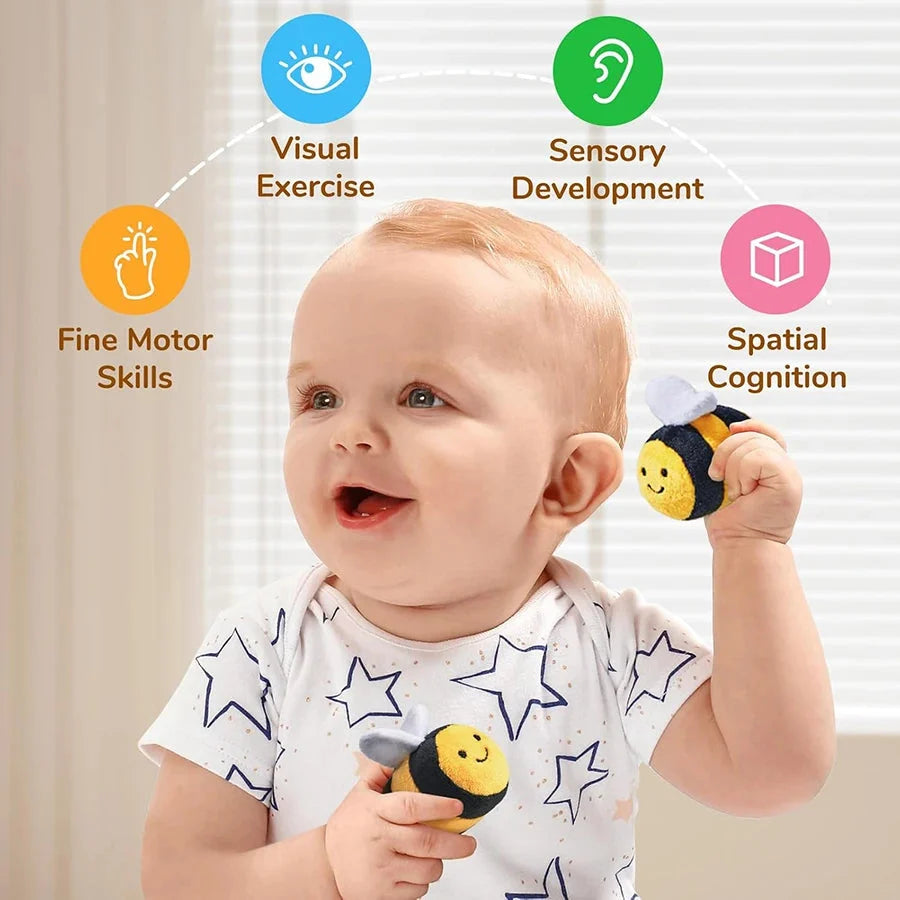 Baby holding a plush yellow beehive sensory toy with smiling bee faces and dangling wings
