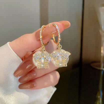 Gold-tone dangling bow earrings with white charm ornaments and rhinestone detail